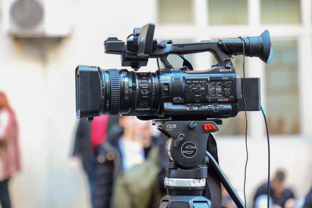 About Close-up of a Sony video camera mounted on a tripod for outdoor filming.